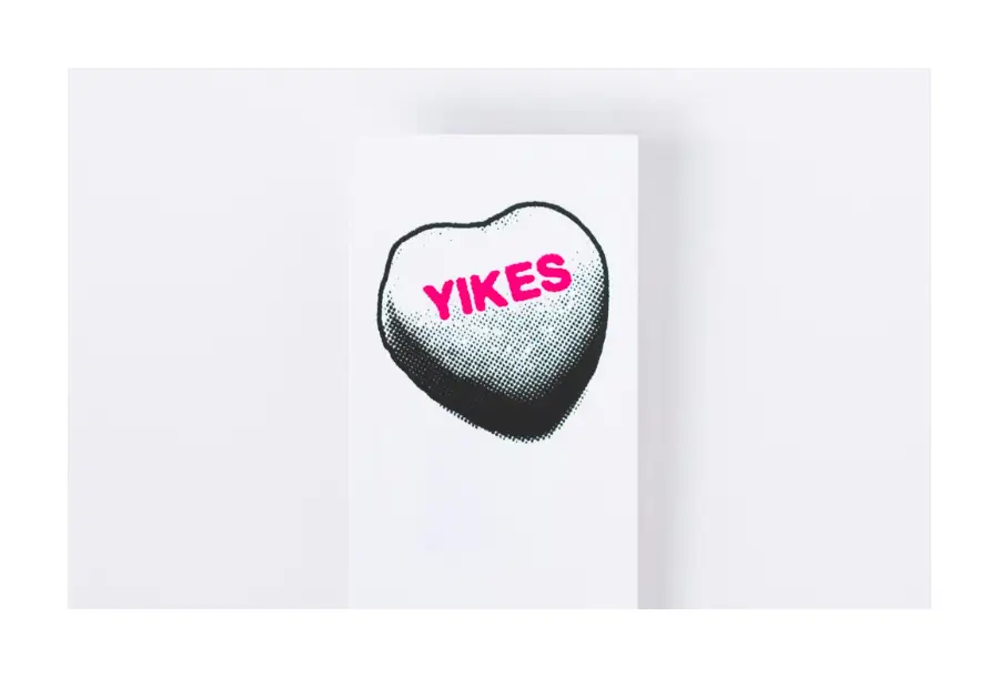 Pictured, a black and white style lolly that is shaded from light to dark, top to bottom. In the centre in bright pink writing is the word "YIKES"